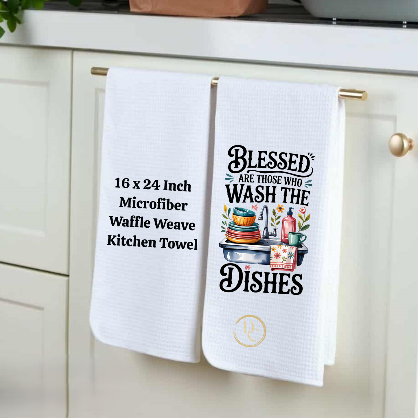 Two white kitchen towels hanging on a cabinet handle, one with text and the other with a graphic design.