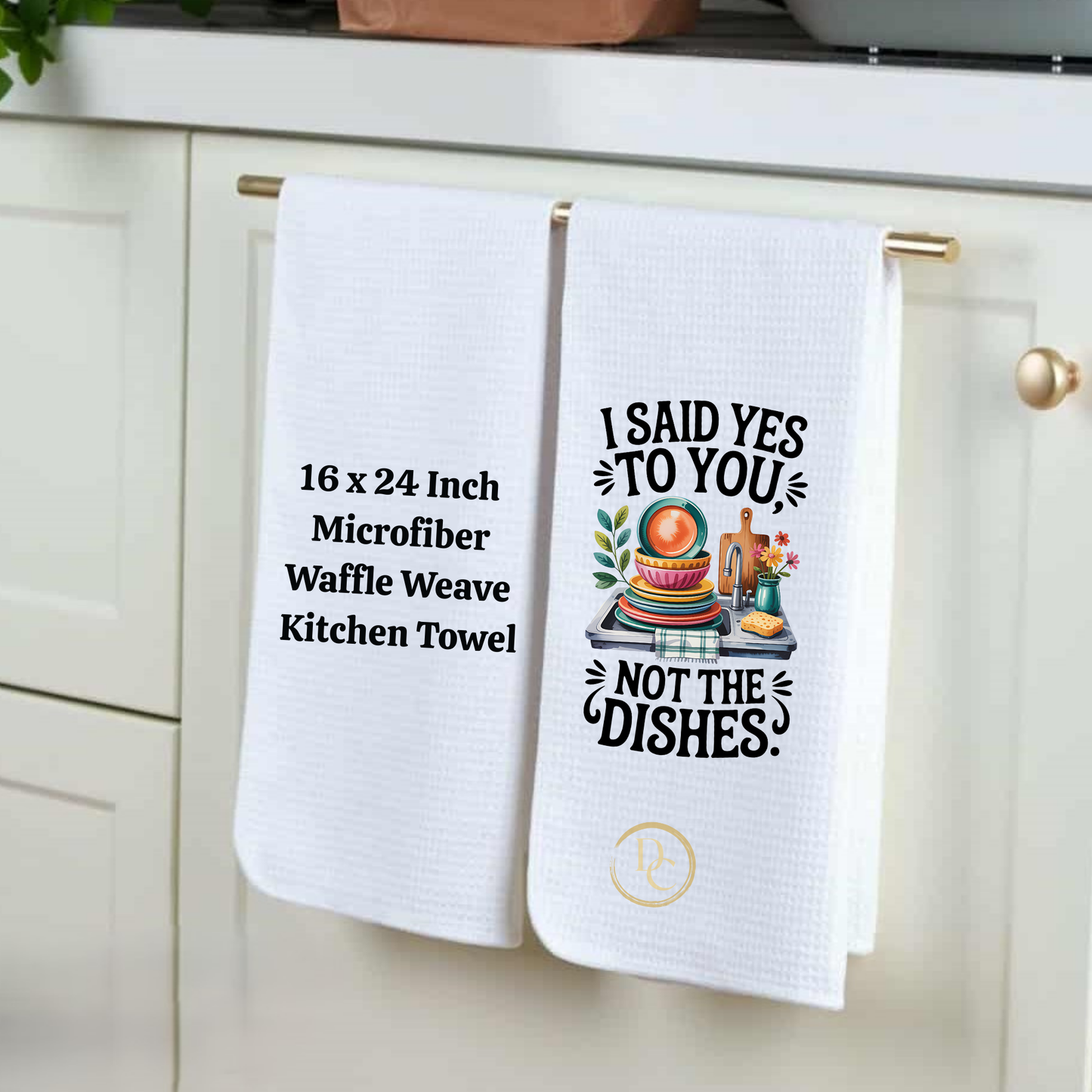 Two kitchen towels hanging on a cabinet handle, one with text and the other with a graphic design.