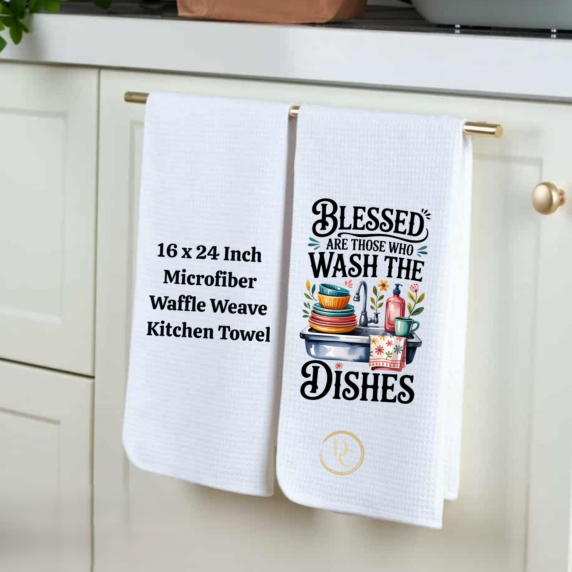 Two white kitchen towels hanging on a cabinet handle, one with text and the other with a graphic design.