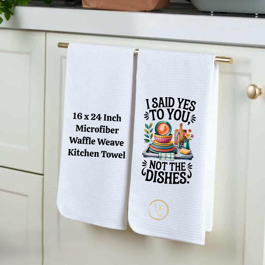 Two kitchen towels hanging on a cabinet handle, one with text and the other with a graphic design.