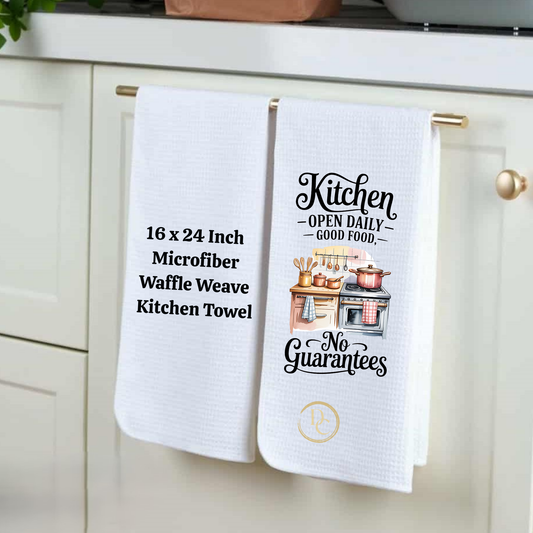 Two white kitchen towels with text and graphics hanging on a cabinet handle.