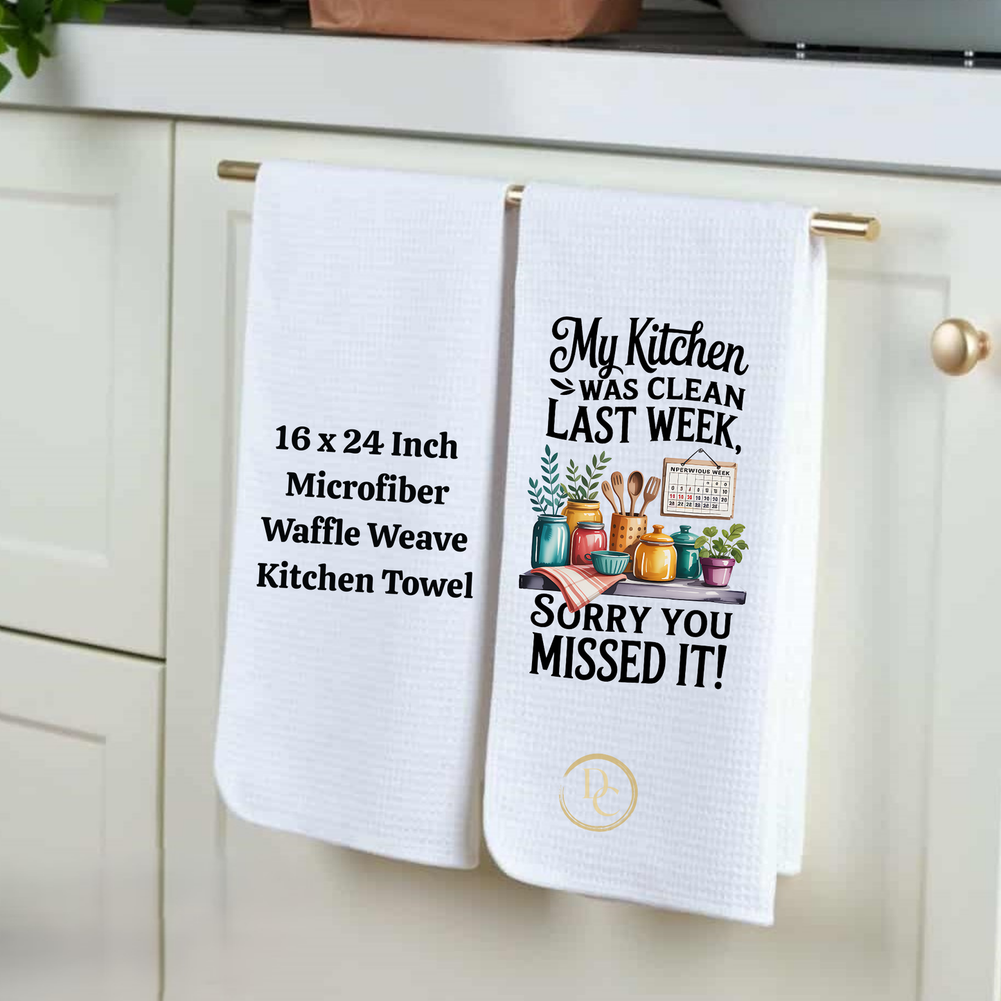 Two white kitchen towels hanging on a cabinet handle, one with text and the other with a graphic design.