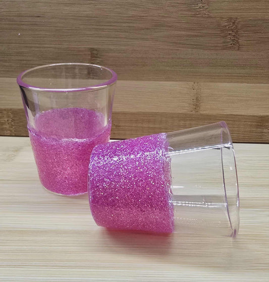 Two Glass shot glasses pink glittery bottoms on a wooden surface